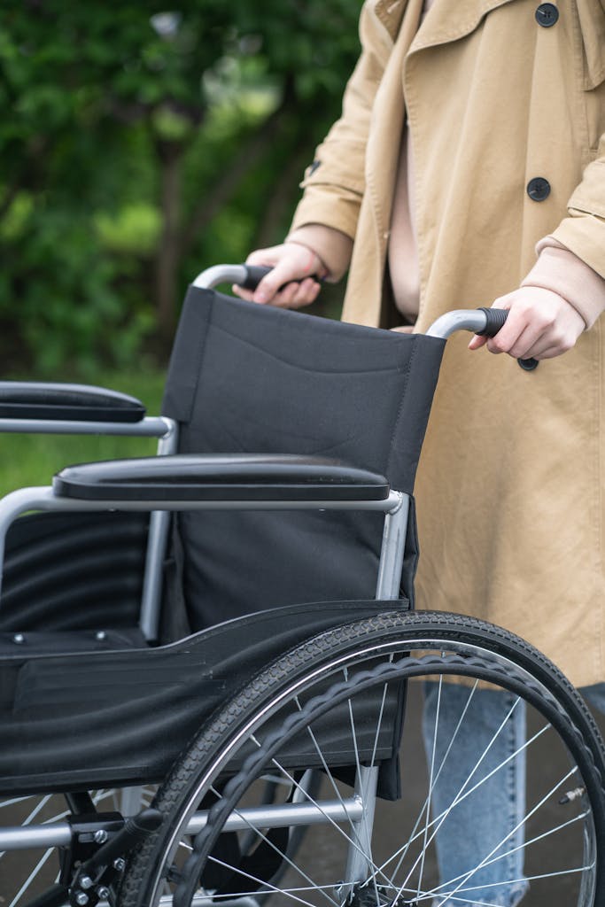 A person in a coat holds the handles of a wheelchair outdoors, illustrating accessibility and support.